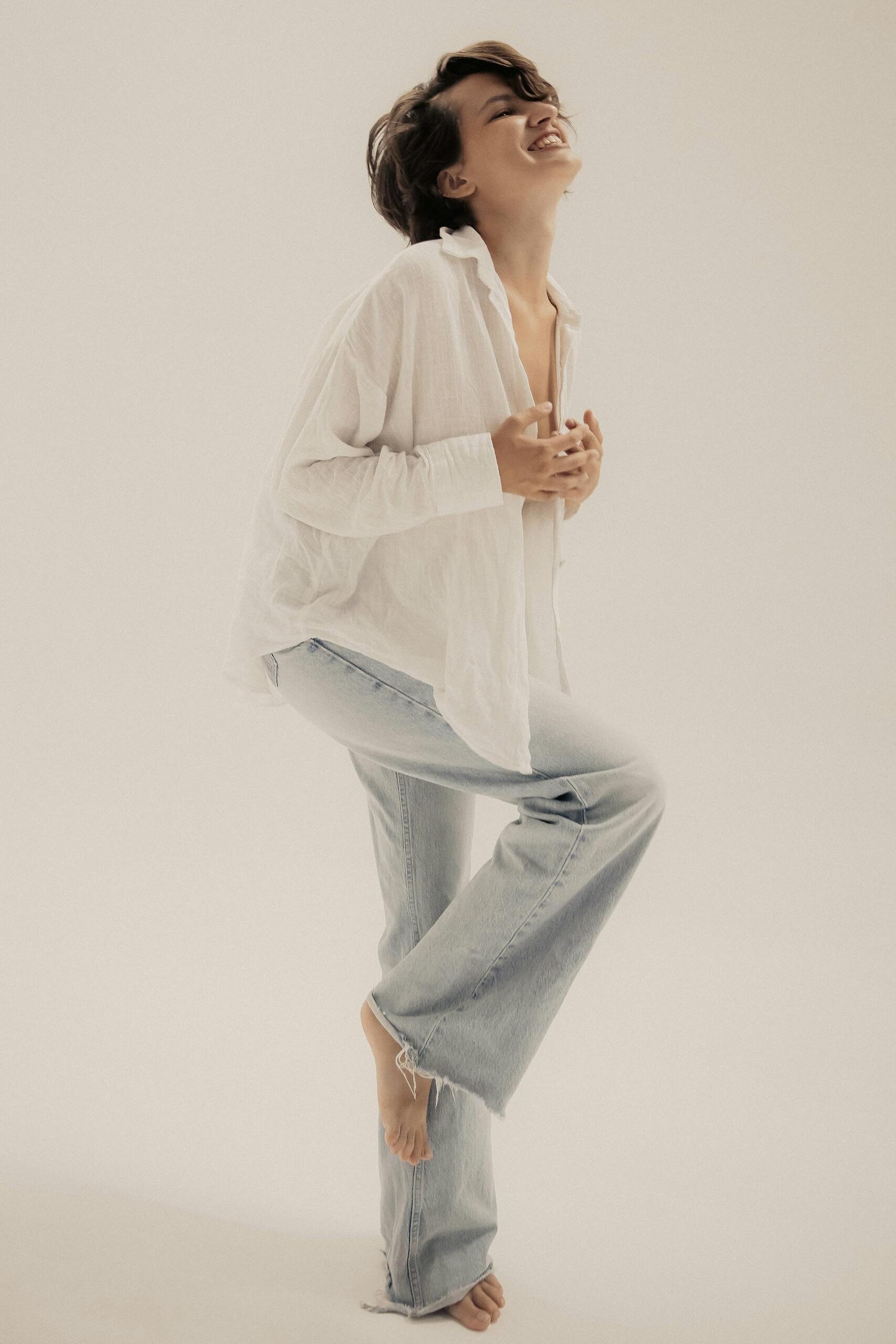 Woman in a relaxed pose with white shirt and jeans in studio setting.